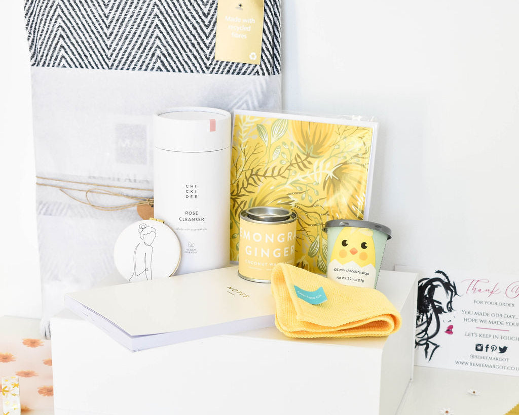 Collection of candles, notebook, and cleanser, mirror, throw and chocolate on a white surface